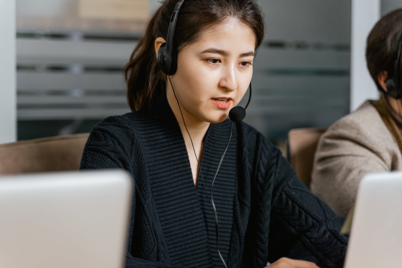 Asian woman in a call center focused on customer support tasks using a laptop.